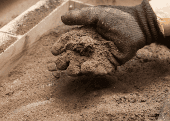Mano con guante colocando cemento en una estructura de construcción en Soria.